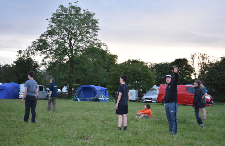 Pupils and staff standing and sitting in the camp, playing a game